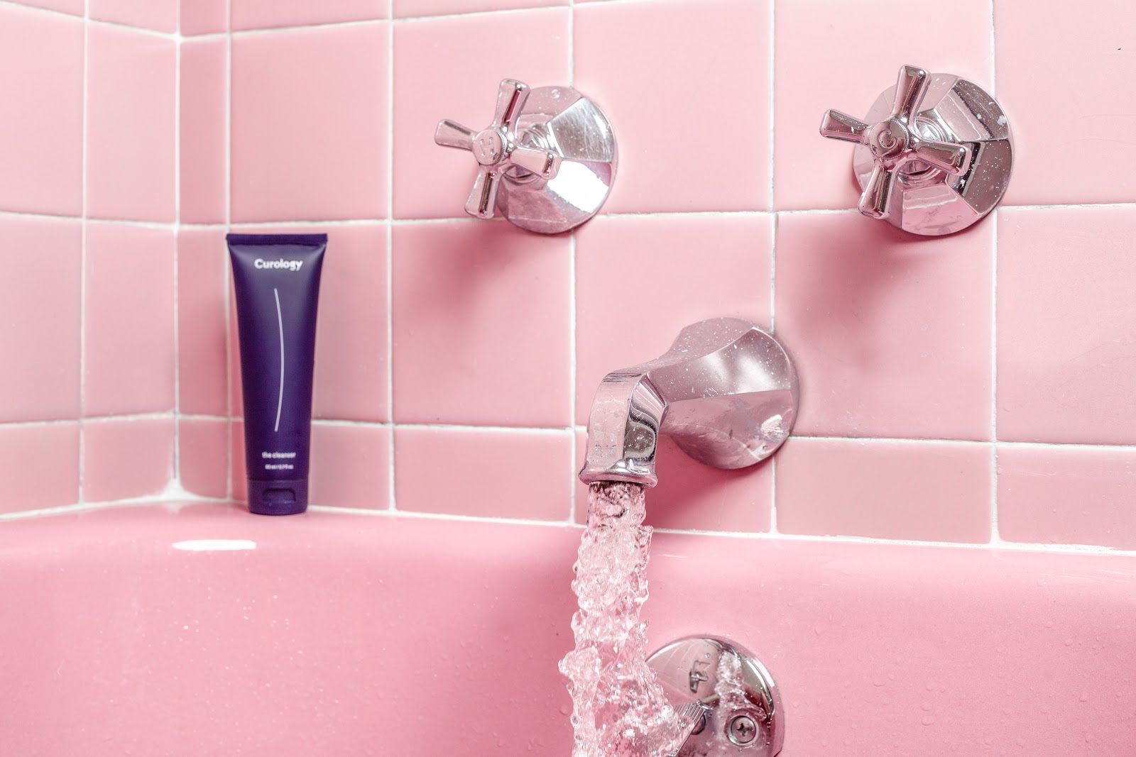 Close-up of a pink tiled bathtub with water running into it.