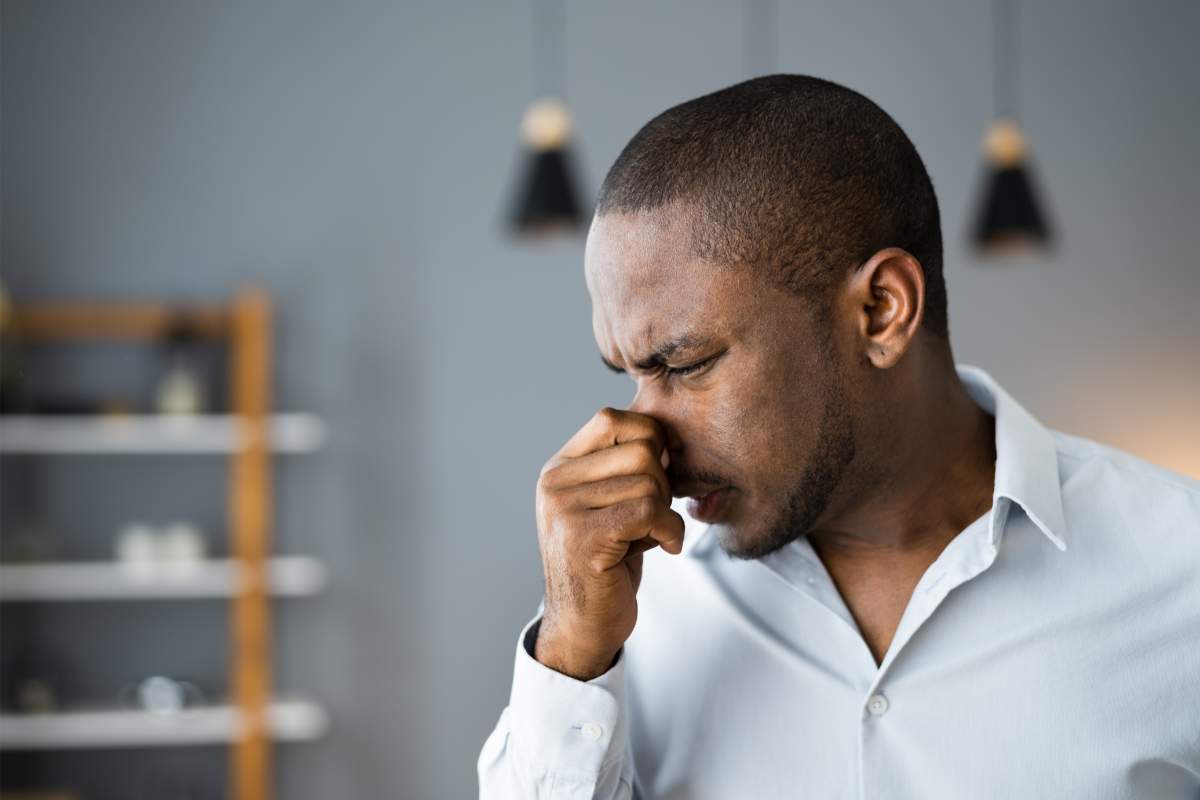 Man standing in a kitchen and holding his nose.