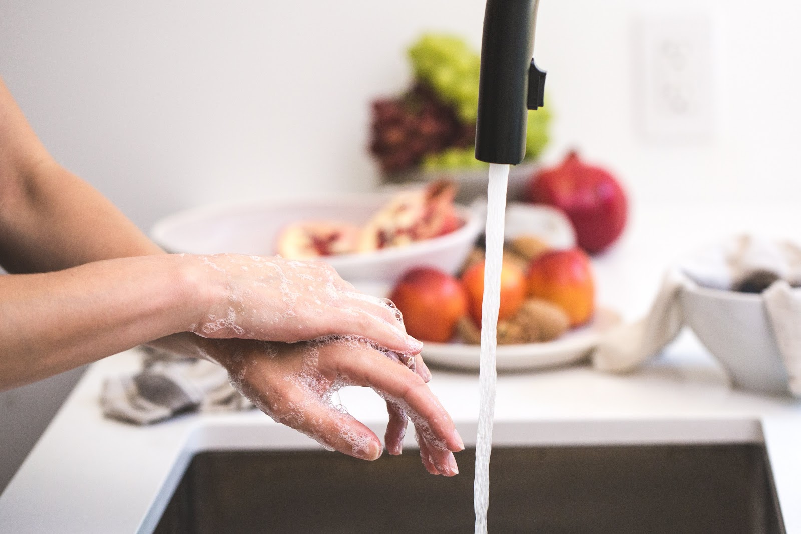 close-up of a pair of sudsy hands beside a running kitchen faucet.